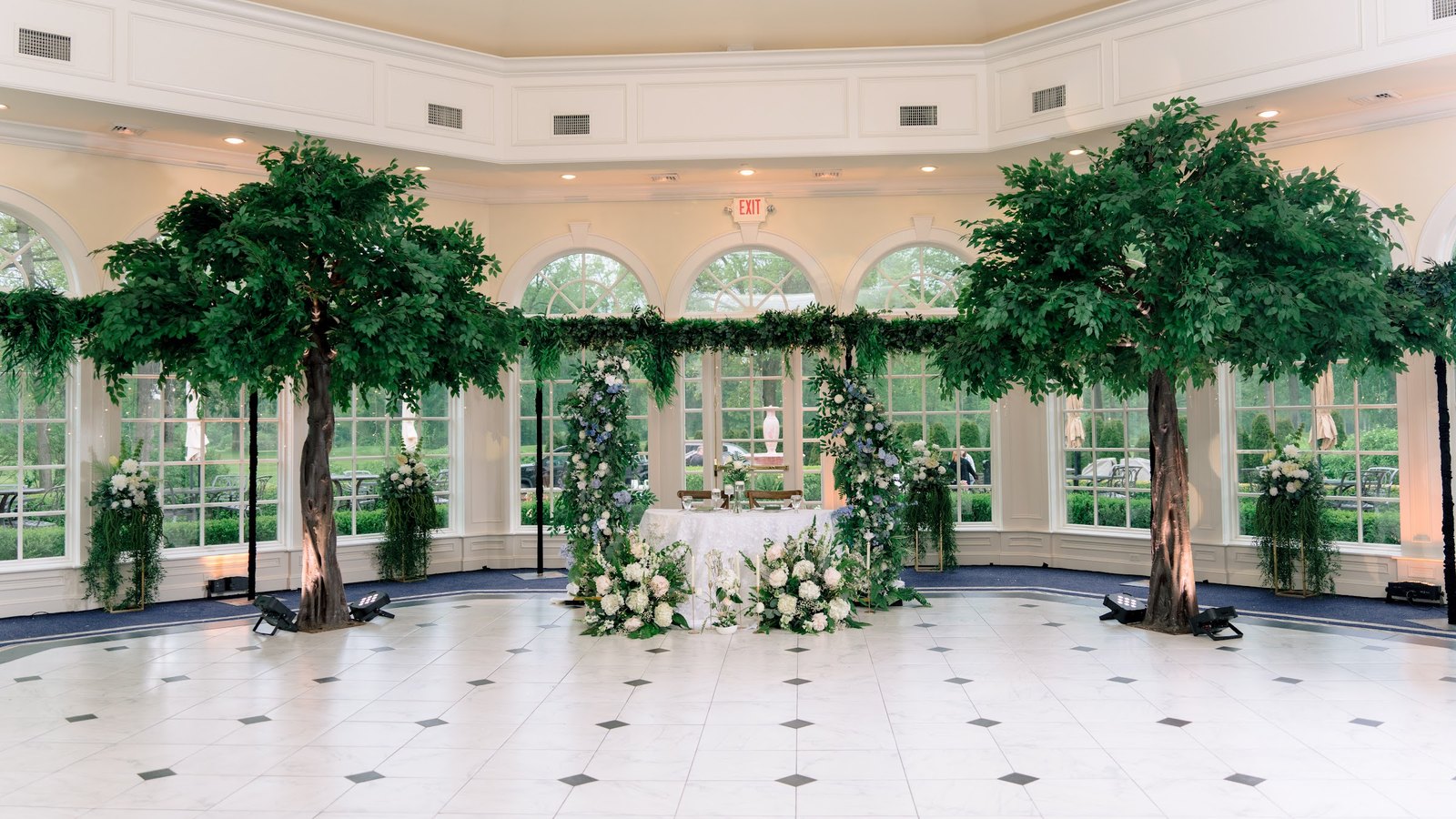 Reception room fully set up with tall trees, a floral sweetheart table and guest tables