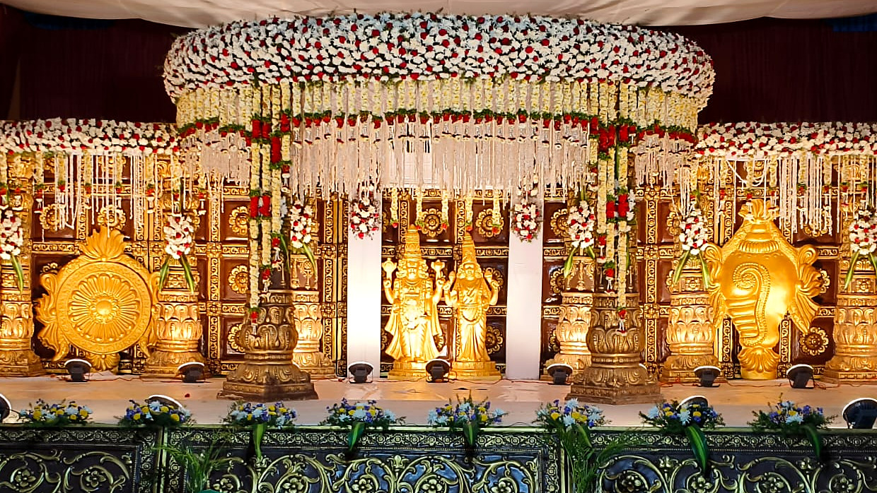 Grand temple-style wedding stage with a jasmine and rose floral canopy, golden deities, chakra and conch